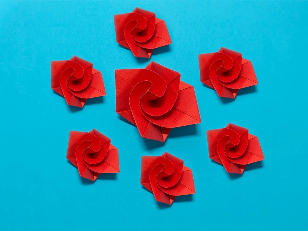 Finché brand non vi separi 5 Origami che mostra delle rose rosse di carta, di varie dimensioni, su un piano azzurro